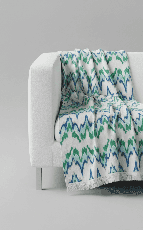 Übergroße Überwurfdecke mit blau-grünem Ikat-Muster und Fransenborte auf weißem Sofa